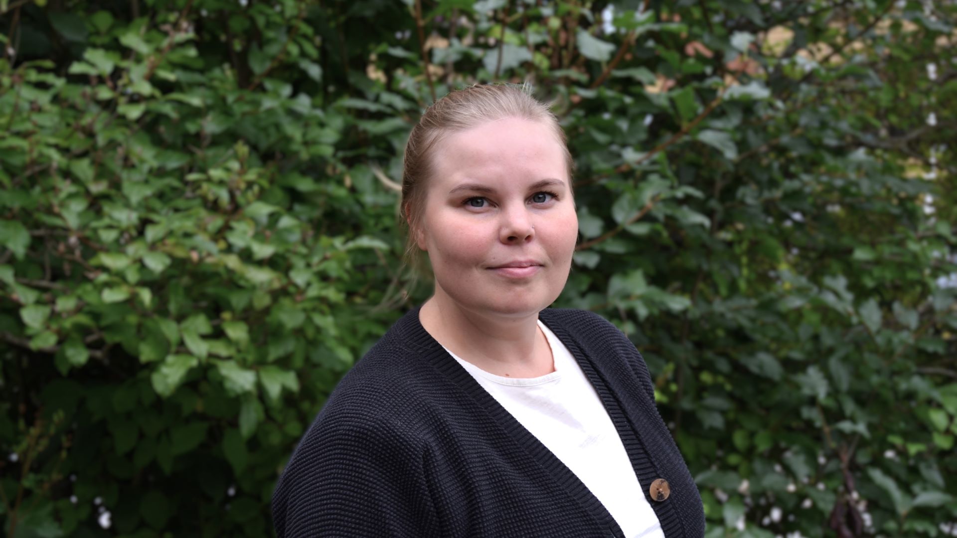 Puolilähikuva naishenkilöstä taustallaan vihreä pensas.