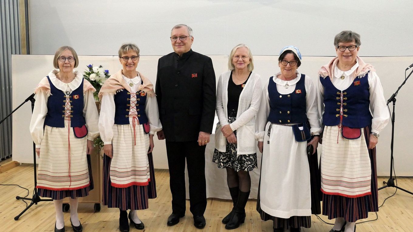 Seisomassa viisi naista, joista neljällä on kansallispuku ja yksi tummiin pukeutunut mies.