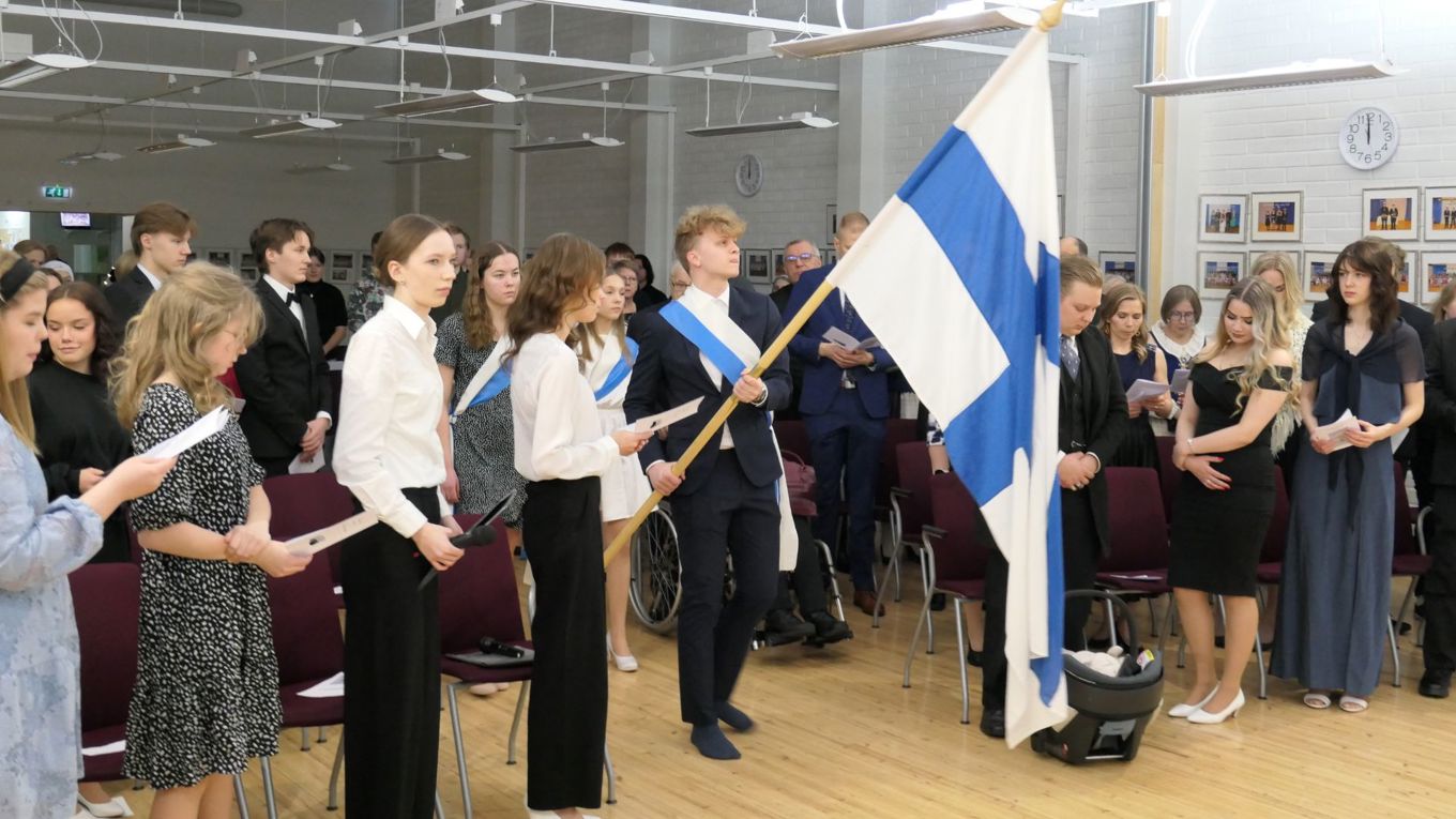 Juhlayleisöä seisomassa kun Suomen lippua kannetaan saliin.