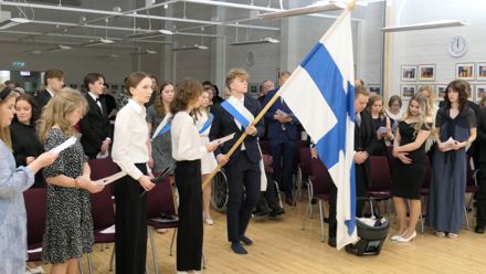 Juhlayleisöä seisomassa kun Suomen lippua kannetaan saliin.