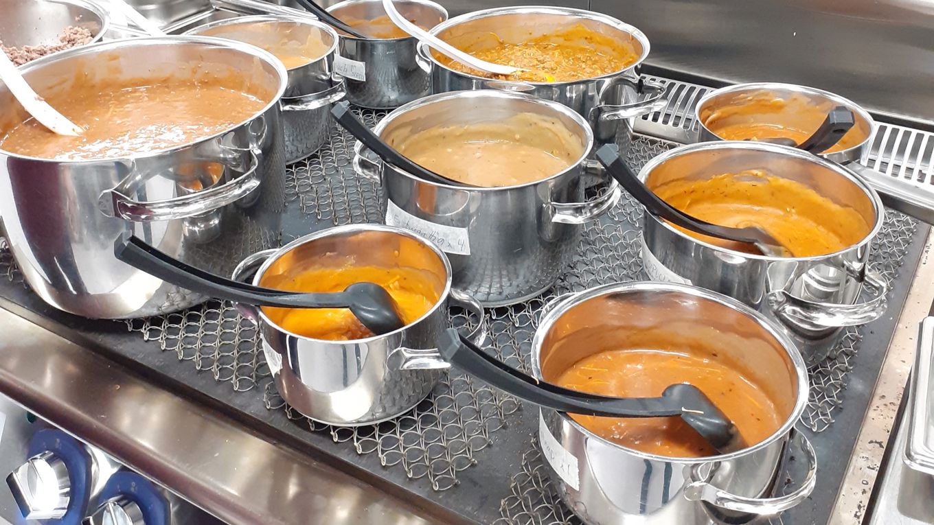 Kuvassa teollisuusliedellä seitsemän kattilaa, joissa oranssinväristä keittoa.