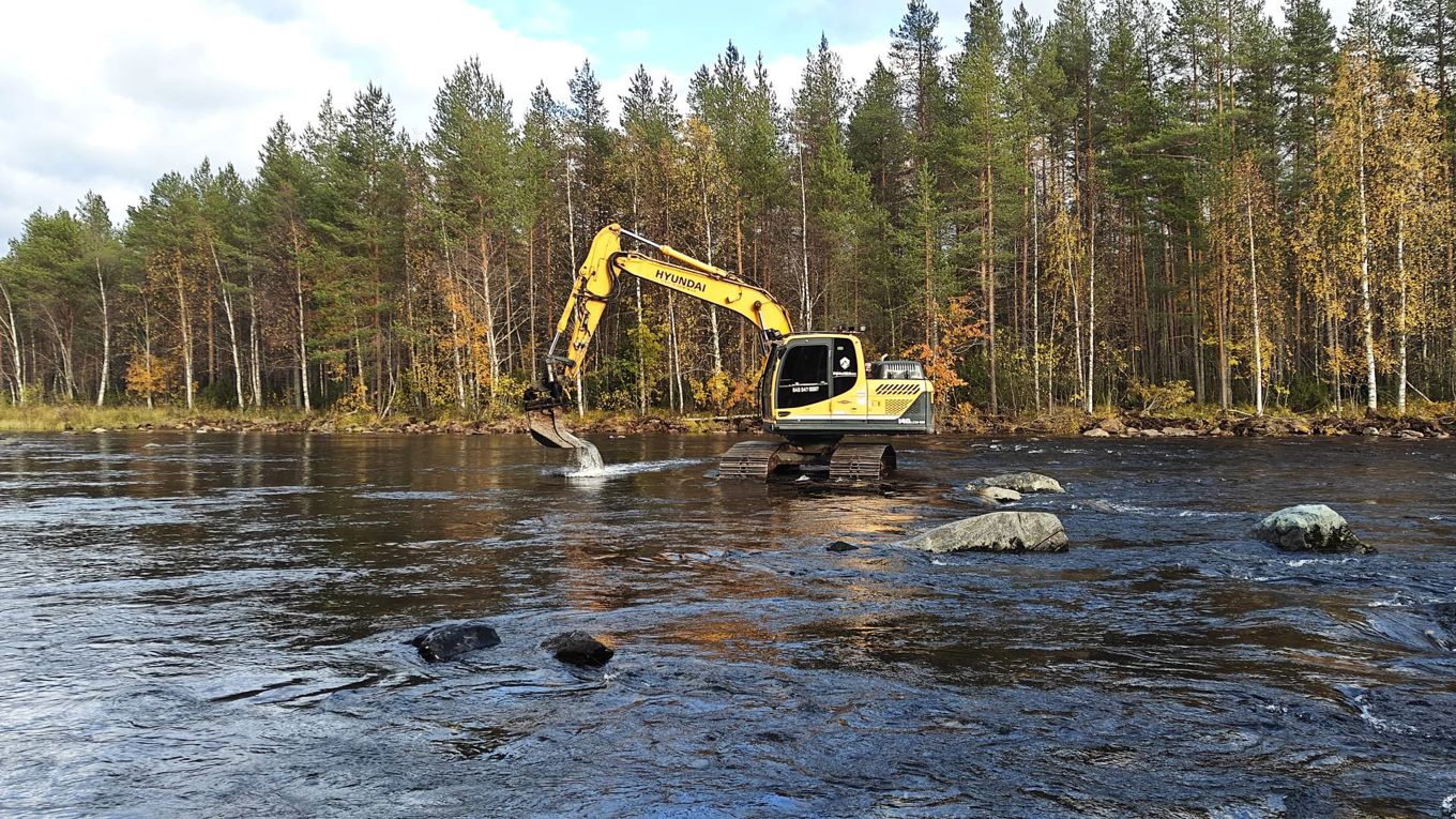 Kaivinkone on joessa ja sen kauhasta valuu vettä.