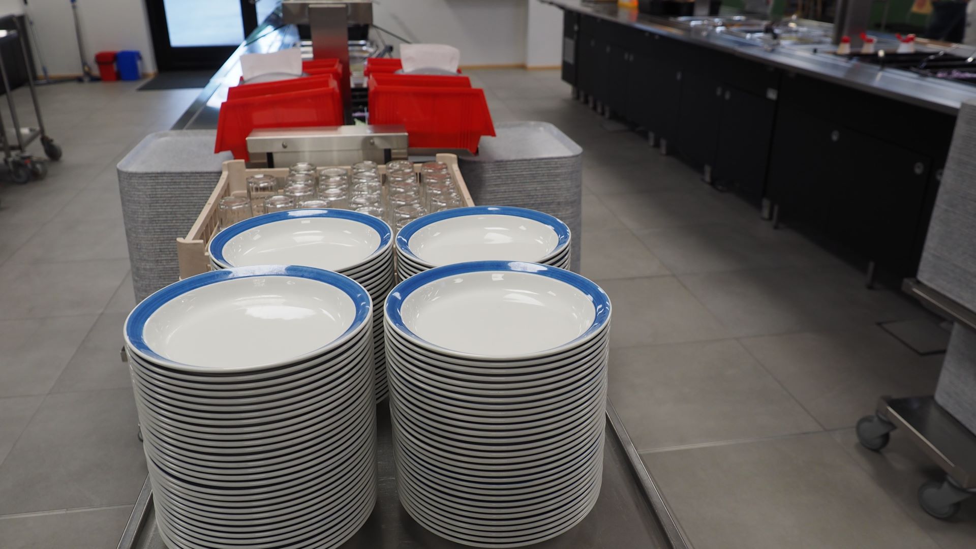 Kuvituskuvassa koulun ruokalan ruokalinjaston alkupäästä, etualalla kaksi pinoa sinireunaisia lautasia